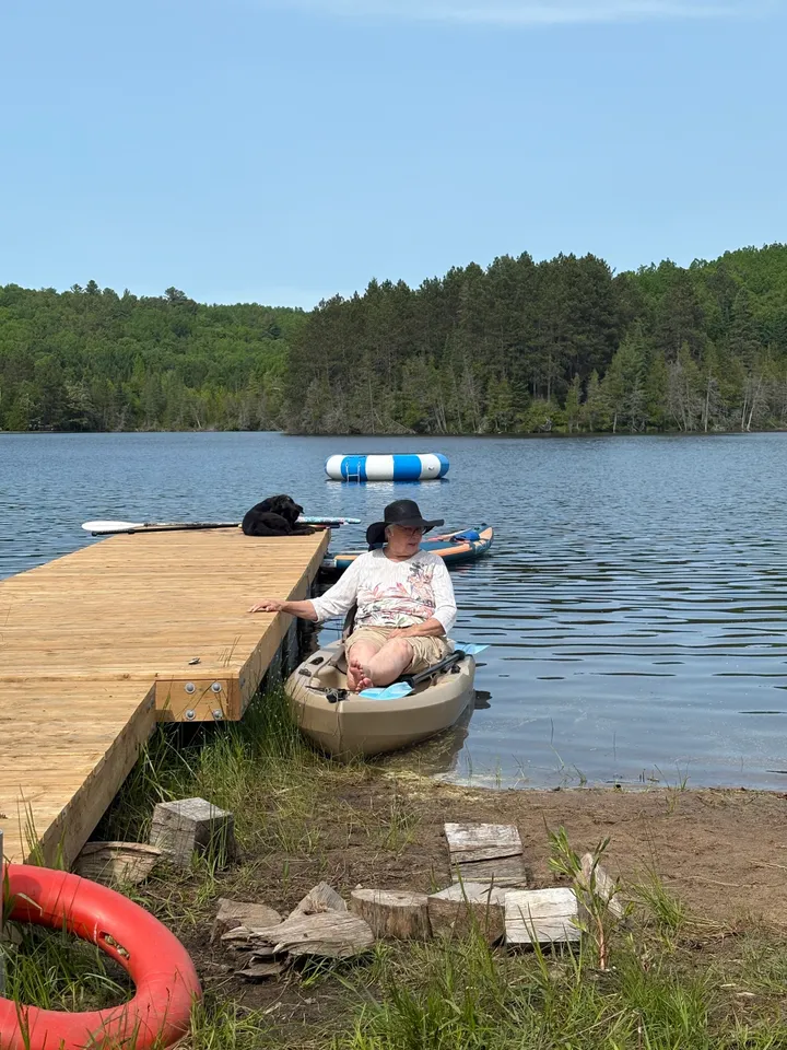Man paddling a kayak near a wooden dock on a lake.